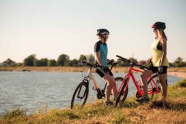 Two women cyclists with bikes standing and talking at the lake shore