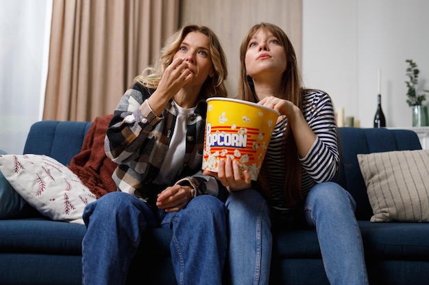 Two women of different ages eating popcorn are concentrated on watching an interesting movie