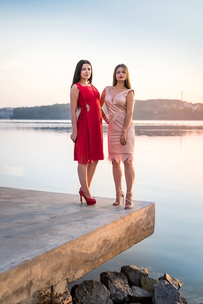 Two women in elegant dresses posing on lakeshore