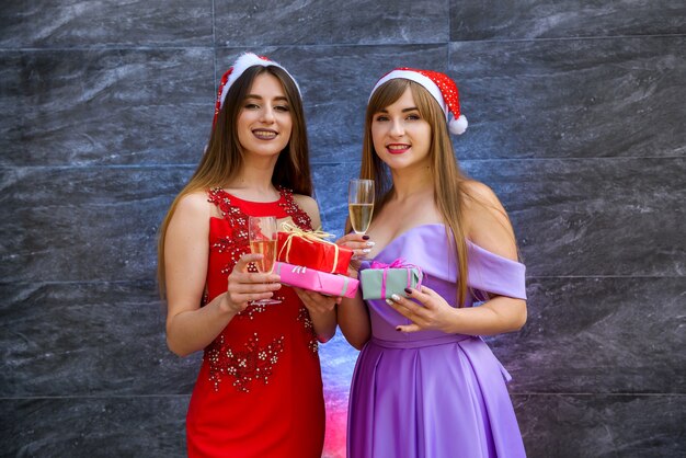 Two women in elegant evening dresses looking in gift bag. New year party celebration