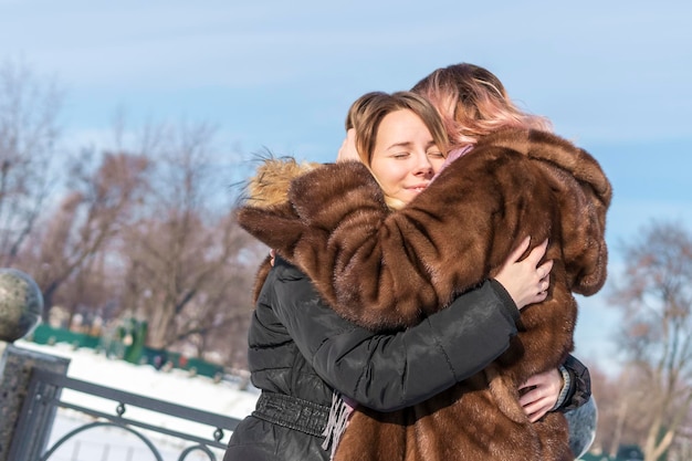 Две женщины нежно обнимаются в зимнем городе у забора