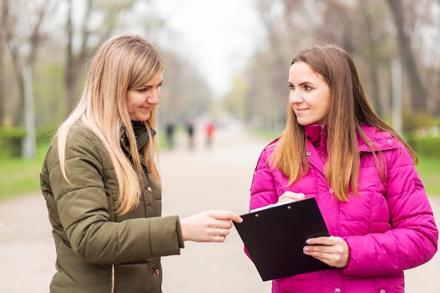 two women engaged in a conversation with a clipboard on a park path