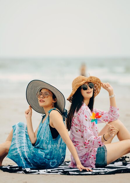 Two Women enjoying beach relaxing joyful in summer by tropical blue water.Model on travel wearing beach hat.