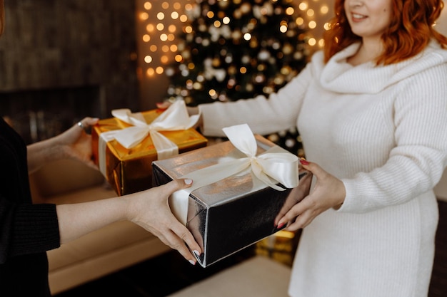 two women exchange Christmas gifts on the background of a Christmas tree