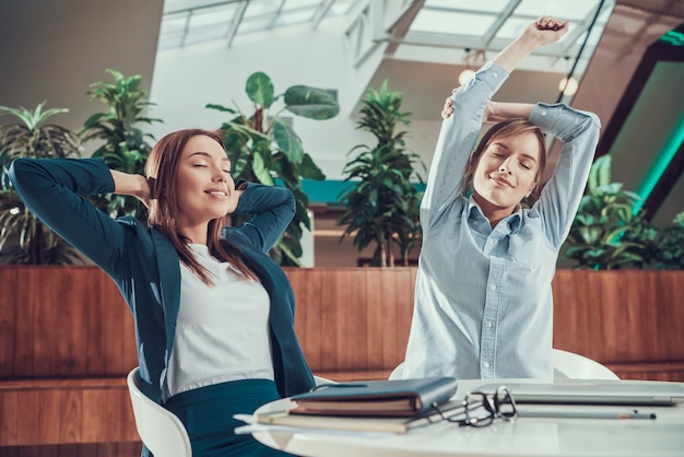 Two women exercising stretching at desk in office.