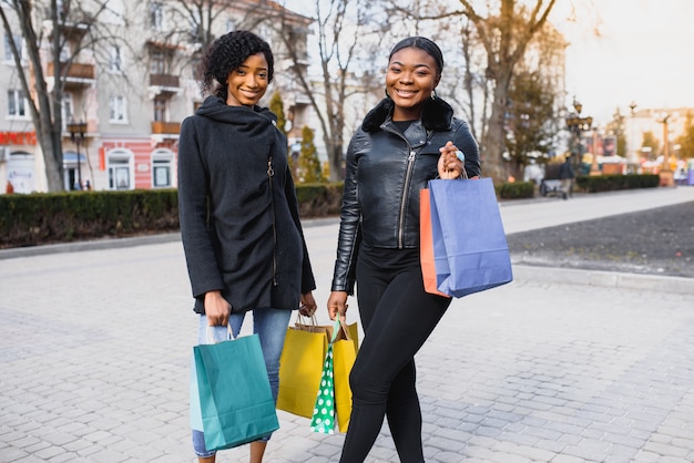 Two women friends in the city on a shopping trip carrying colorful shopping bags.