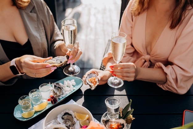 Two Women friends eating fresh oysters and drinking chilled prosecco wine on the summer sunset in restaurant Seafood delicacies