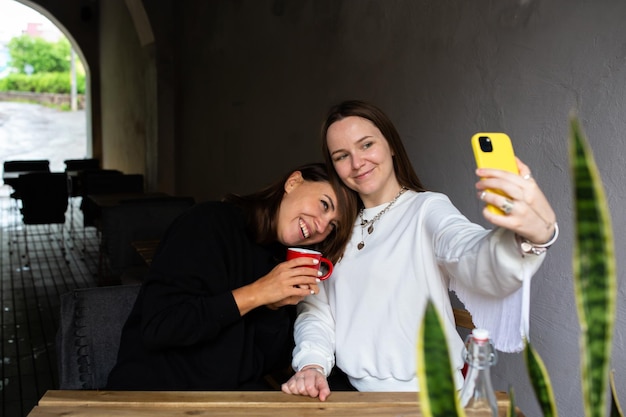 Due amiche si divertono all'aperto nella caffetteria e si fanno un selfie su uno smartphone