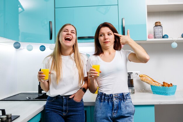 Due amiche in piedi in cucina e bevono succo d'arancia. le amiche chiacchierano e condividono segreti in cucina, a colazione