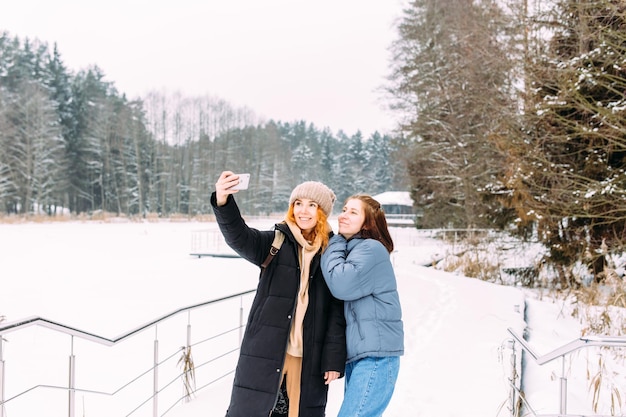 Two women friends in winter with a phone takes a selfie in winter