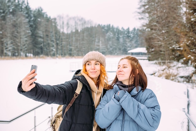 Two women friends in winter with a phone takes a selfie in winter