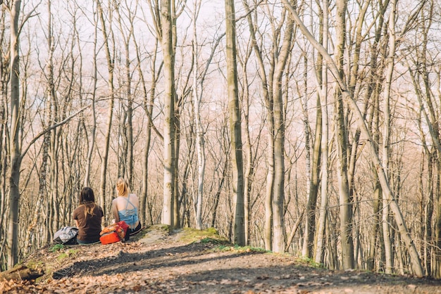 Two women girlfriends sitting on the ground at the cliff in forest