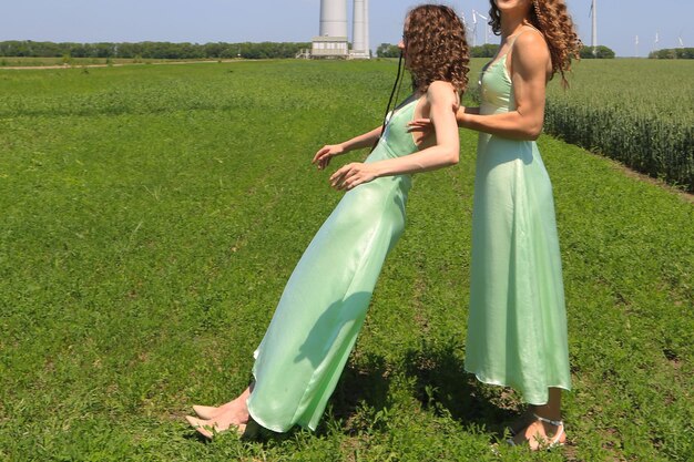 Two women in green dresses are dancing in a field