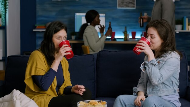 Two women hanging out at home party giving hight five while relaxing on sofa