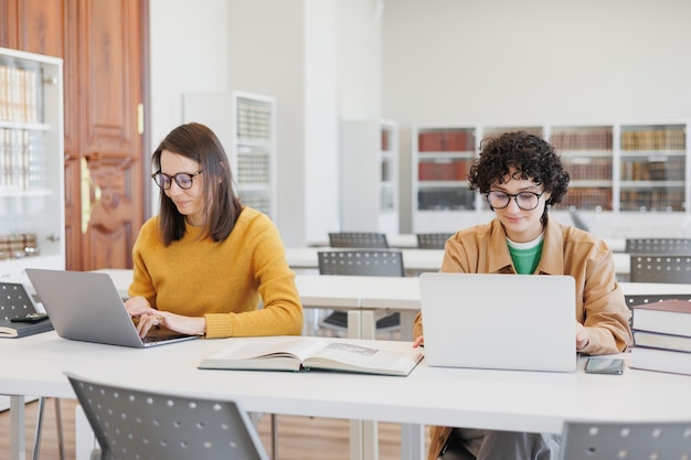 写真 図書館や共同作業をしている 2 人の女性が向かい合って座ってラップトップで作業している