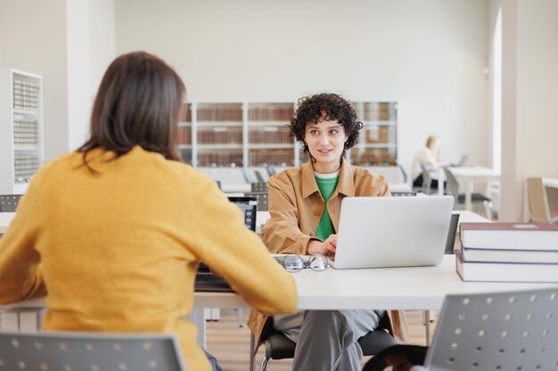 사진 도서관이나 직장에 있는 두 명의 여성이 서로 반대편에 앉아 노트북 작업을 하고 있습니다.