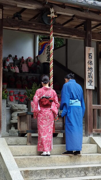 写真 伝統的な着物を着た 2 人の女性が、正面に中国語の文字が書かれた寺院の前に立っています。