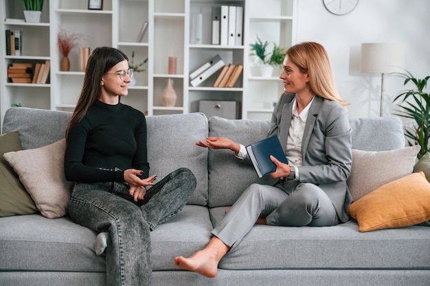 two women is sitting on the sofa and talking casual and formal clothes