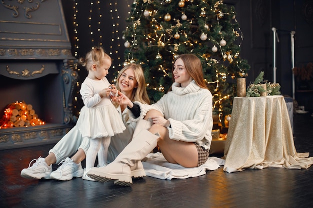 Two women and little girl sitting on a floor near Christmas tree