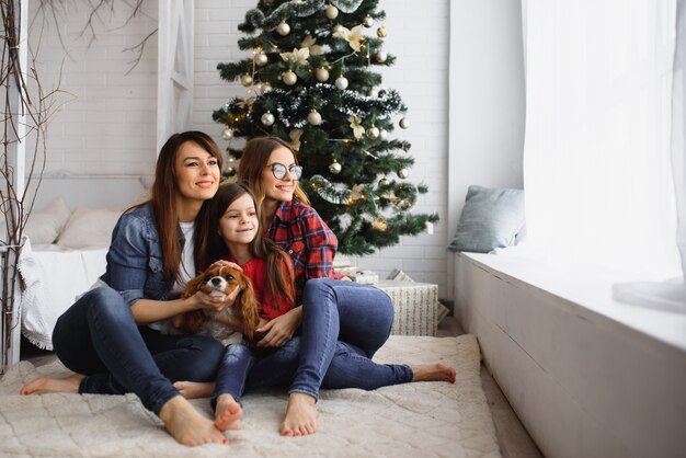 クリスマスツリーの近くで抱き締める犬と2人の女性と少女