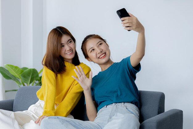 Two women in the living room they are waving to their friends in a smartphone video calling program they are spending their vacations watching movies and listening to music together