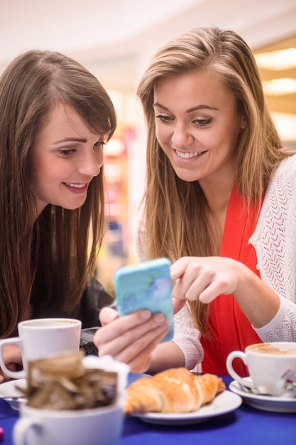 Two women looking at mobile phone while having snacks and coffee