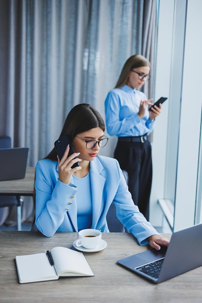 Two women in the office are working and doing business Business woman in office with glasses and phone Woman manager in glasses and shirt in the office Head of working day