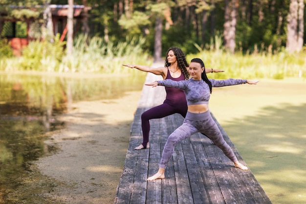 Two women practicing yoga doing the exercise virabhadrasana warrior pose training