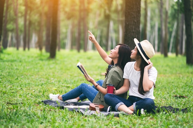 Two women reading book together while sitting and looking into the woods