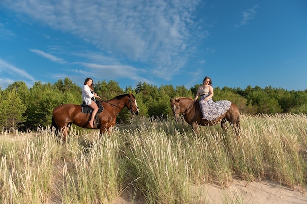 Two women riding horses on a beach next to a forest