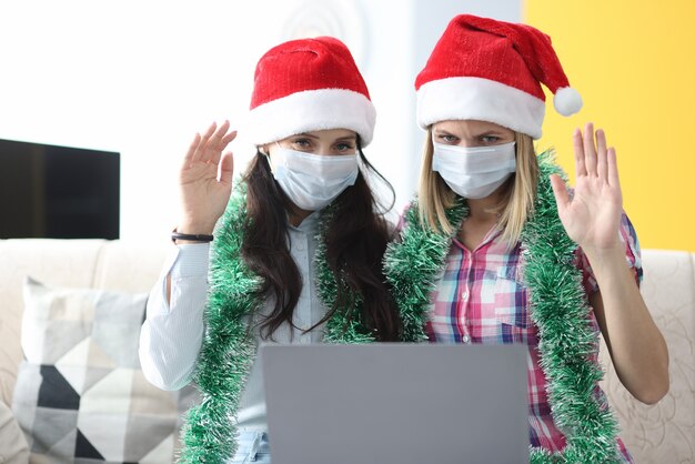 Two women in santa claus hats waving to laptop.