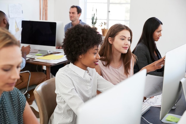 Two women sat at a computer discuss work in open plan office