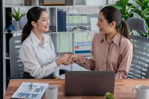 Two women shaking hands in an office, one of them is wearing a white shirt and the other is wearing a white shirt.