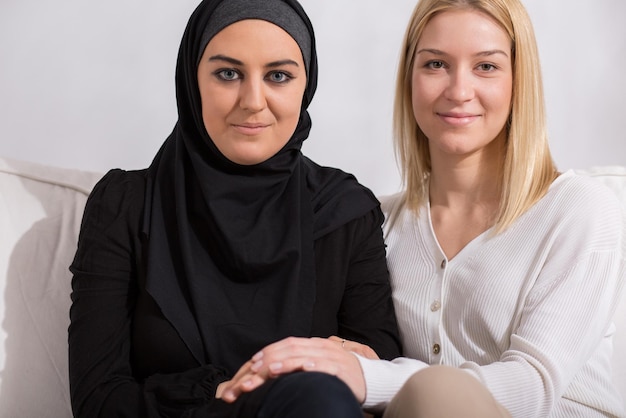 Two women sit on a couch, one of them is wearing a hijab and the other is wearing a hijab.