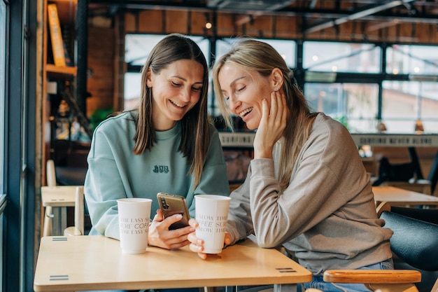 two women sitting in a coffee house and laughing use the phone for online communication