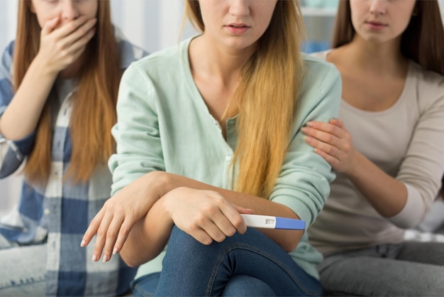 Two women sitting on a couch, one of them has a pregnancy test.