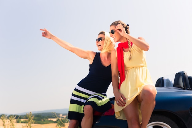 Two women sitting on hood of convertible car 