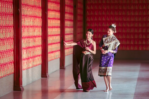 Две женщины в тайских национальных костюмах и лаосском национальном костюме во время посещения туристических достопримечательностей в Таиланде