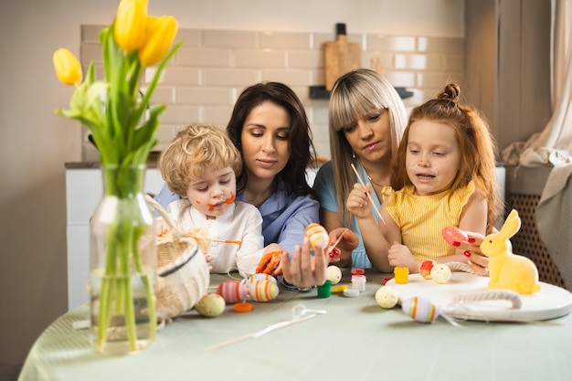 Two women their little children decorate Easter eggs