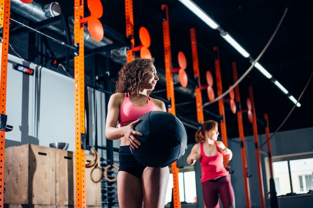 Two women throws medicine balls in fitness gym