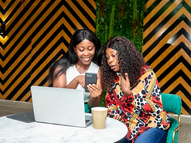 Two women using laptop computer checking their mobile phone in a coffee shop