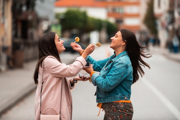 Two women walking around modern town and eating fresh poffertjes. Selective focus. High quality photo