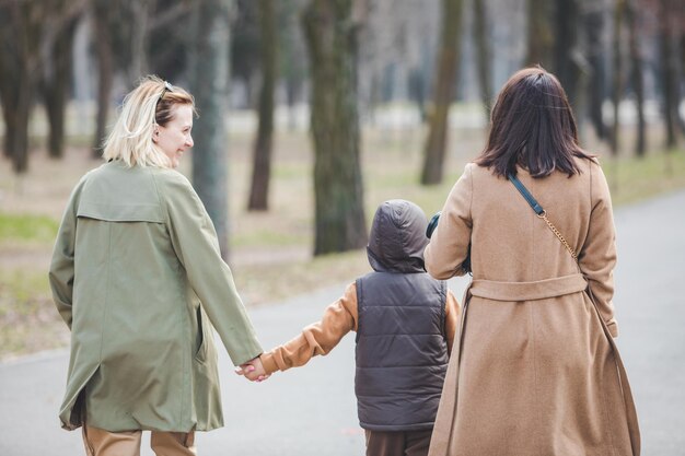 小さな子供の秋の季節と都市公園を歩いている2人の女性