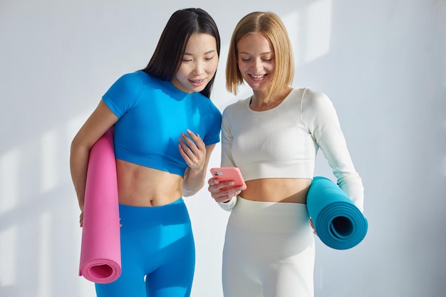 Two women watching yoga poses on smartphone while doing yoga Concept of physical and mental health care asian and caucasian ethnicity