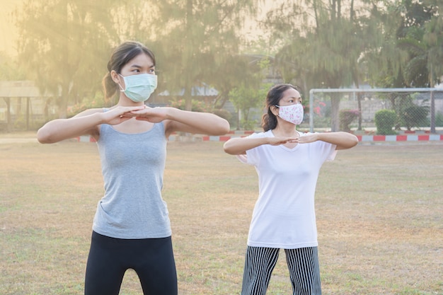 Foto due donne che indossano maschere che esercitano la mattina nel parco e la natura solare. e buona salute per il nuovo stile normale e di vita