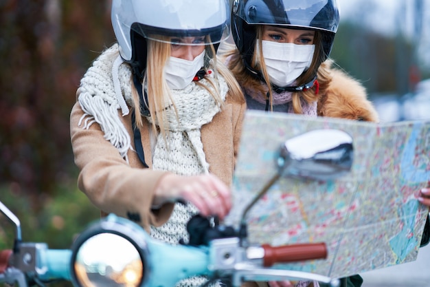 two women wearing masks and holding map while commuting on scooter