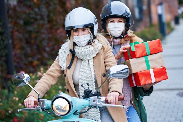 two women wearing masks and holding shopping bags commuting on scooter