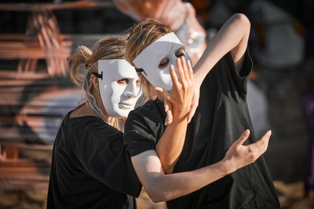 芸術演劇祭で踊る白い劇場マスクの2人の女性完全な黒い服のスタイルの2人の女の子ダンサーの野外ダンスパフォーマンス野外芸術演劇祭