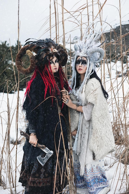 two women witches in fantasy clothes and crowns standing in winter snow