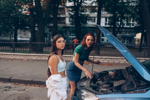 Two women with broken car on the road Open hood